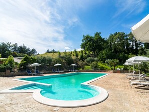 A rectangular swimming pool with a tiled edge, surrounded by a brick patio. There are lounge chairs and umbrellas along the poolside. - Secluded Mansion in Perugia with Hot Tub (Perugia)