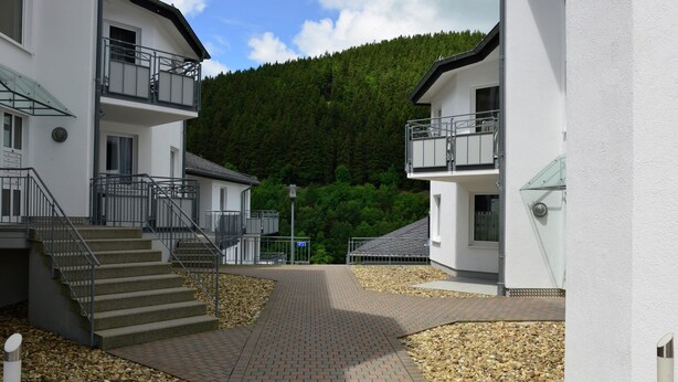 A modern building with a central courtyard, surrounded by white walls and a forested hillside. - Modernes Apartment in Willingen mit Balkon (Willingen)