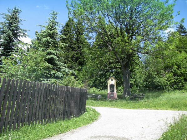 A rural road with a wooden fence on one side and a small chapel-like structure in the distance. - Spacious Hill-view Villa (Rajcza)