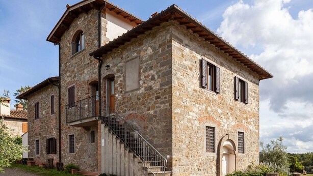 Un edificio de piedra con una escalera que lleva a un nivel superior, un balcón pequeño y una puerta con ventanal.