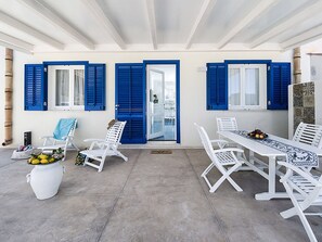 A covered outdoor area with white furniture, blue shutters, and a glass door leading to a pool. - Belvilla by OYO Spuma di Mare - Riccio (San Vito Lo Capo)