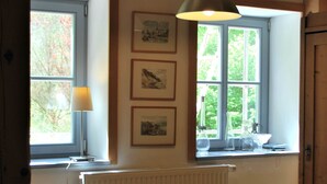 A room with a large window, a radiator, a wicker chair, and a table with a lamp. - Watermill Stay With Garden (Heringen)