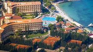 Vista aérea de un hotel costero con varias edificaciones, una piscina y una zona de playa.