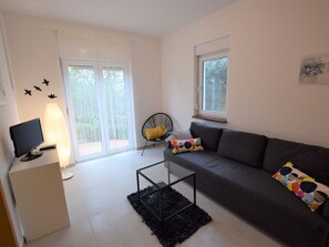 A modern living room with a grey sofa, a black armchair, a glass coffee table, and a TV on a stand. - Home With a Private Terrace in a Quiet Area, Near the Sea (Kolan)
