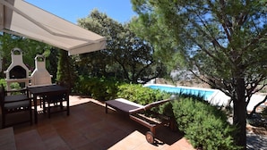 Une terrasse avec un barbecue, une table et des chaises, une piscine et un arbre.