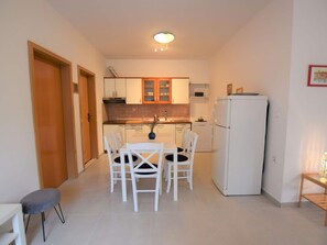 A compact kitchen with white cabinets, a white refrigerator, and a dining table with chairs. - Home With a Private Terrace in a Quiet Area, Near the Sea (Kolan)