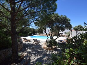 A pool area with lounge chairs, surrounded by trees and a stone wall. - Home With a Private Terrace in a Quiet Area, Near the Sea (Kolan)