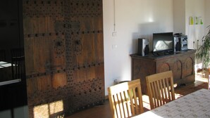 Un comedor con una mesa de madera, sillas, un televisor sobre un mueble y una puerta grande de madera.