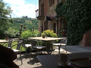 An outdoor patio with a table and chairs, surrounded by greenery and a view of a hilly landscape.
