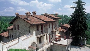 A stone house with a tiled roof, a balcony, and a large tree nearby. - Mansion in Langhe With Pool and Winery Charm (Bastia Mondovì)