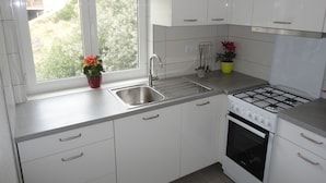 Una cucina moderna con mobili bianchi, un lavello in acciaio inossidabile, un fornello a gas e una finestra con vista sul verde.