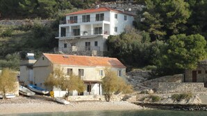 Un edificio costiero con tetto in tegole rosse, un balcone e un muro in pietra.