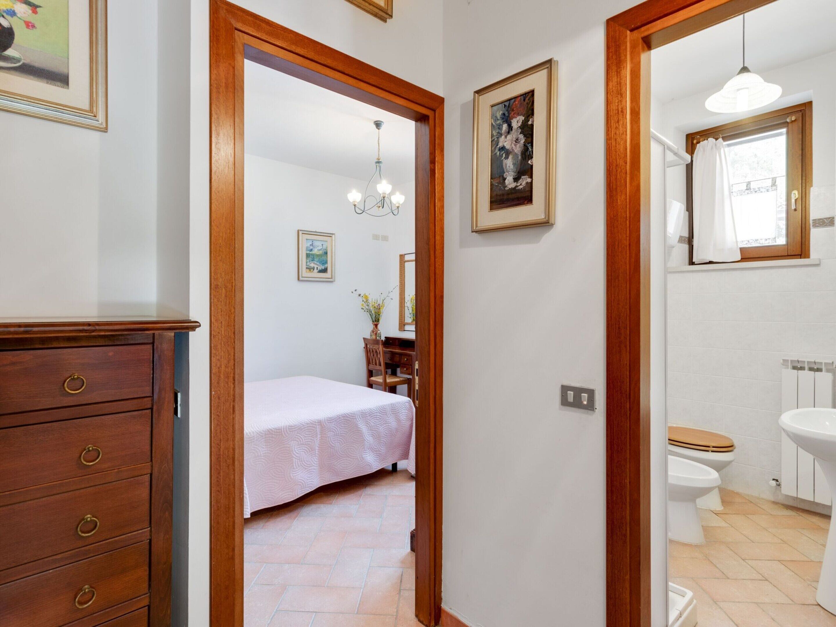 A bedroom with a bed, wooden dresser, and a hallway leading to a bathroom with a toilet and sink.
