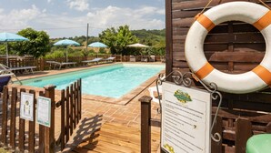 Un espace piscine doté d’une terrasse en bois, de chaises longues et d’une bouée de sauvetage accrochée à la clôture.