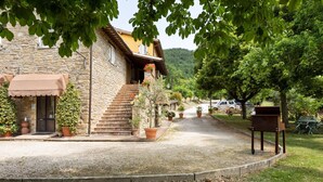 Un bâtiment en pierre avec un escalier menant à un balcon, entouré de gravier et de plantes en pot.