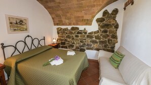 A bedroom with a bed, a nightstand, a stone wall, a painting, and a sofa. - Apartment in a Rustic House in the Tuscan Hills Near the Sea (Monterotondo Marittimo)
