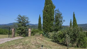 A rural landscape with tall cypress trees, a stone gate, and a clear blue sky. - Apartment in a Rustic House in the Tuscan Hills Near the Sea (Monterotondo Marittimo)