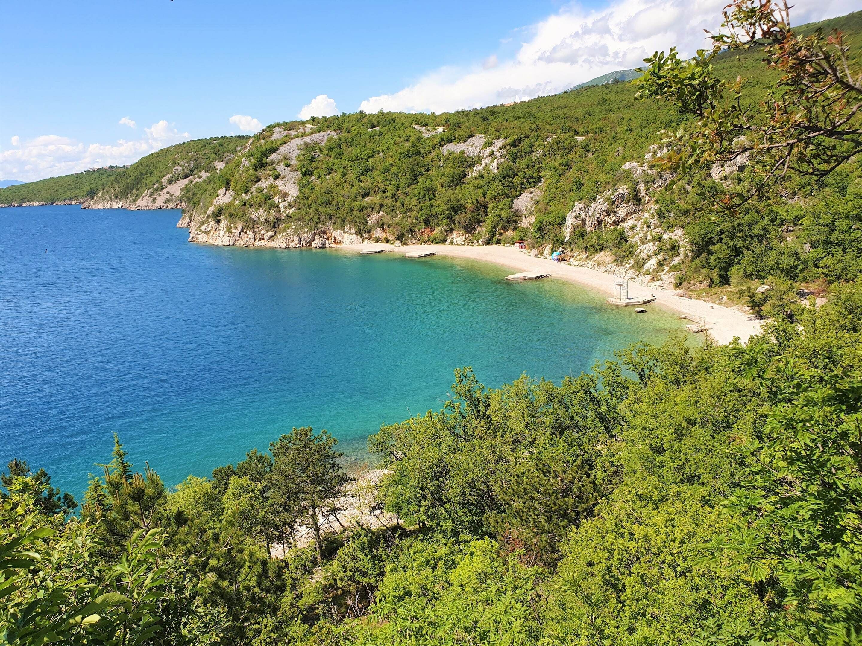 A coastal landscape with a beach, clear blue waters, and dense greenery.