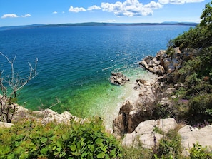 A coastal landscape with clear blue waters, rocky shores, and greenery.