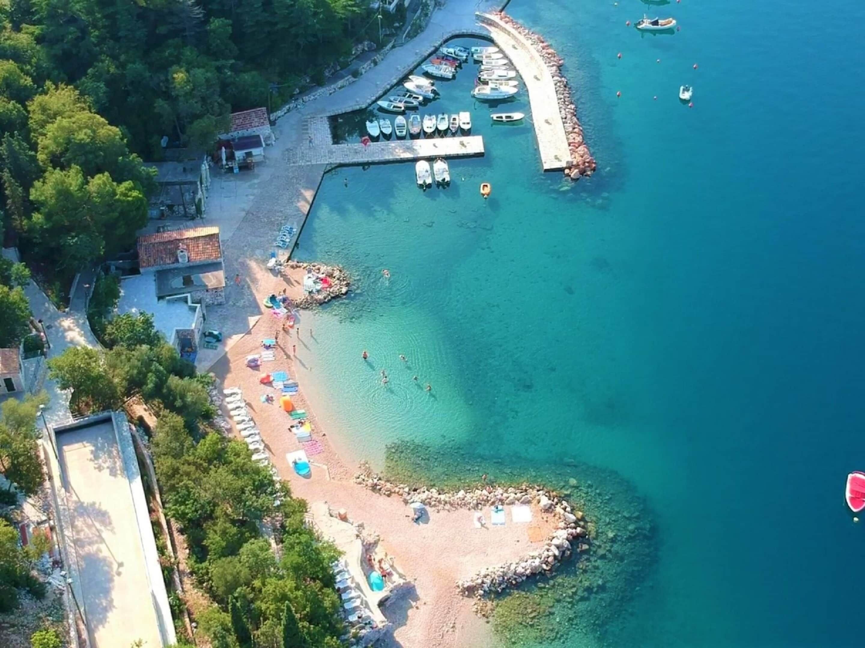 An aerial view of a coastal area with a beach, boats, and a pier.