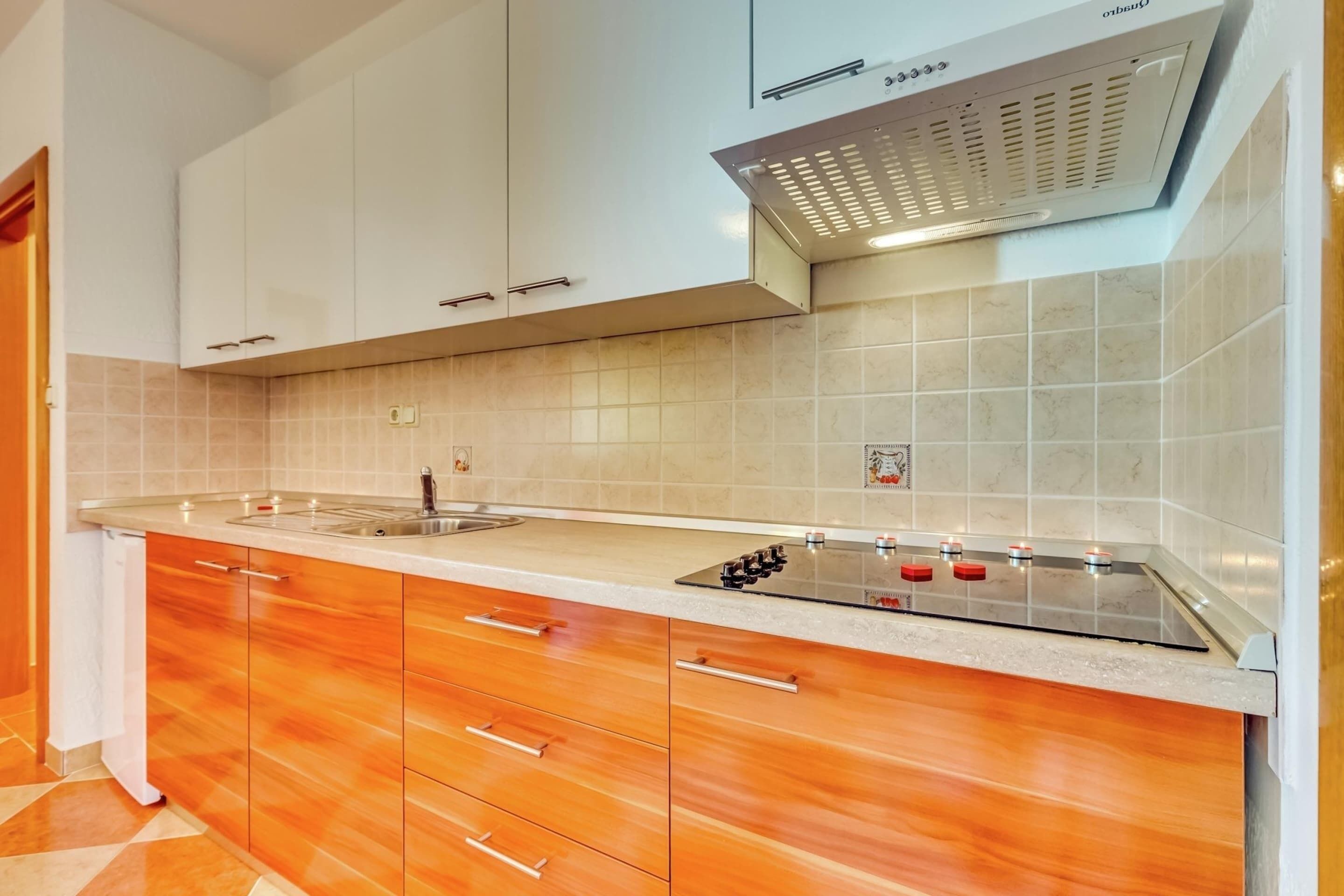 Una cucina moderna con mobili bianchi, un piano cottura in acciaio inossidabile e una parete rivestita di piastrelle.