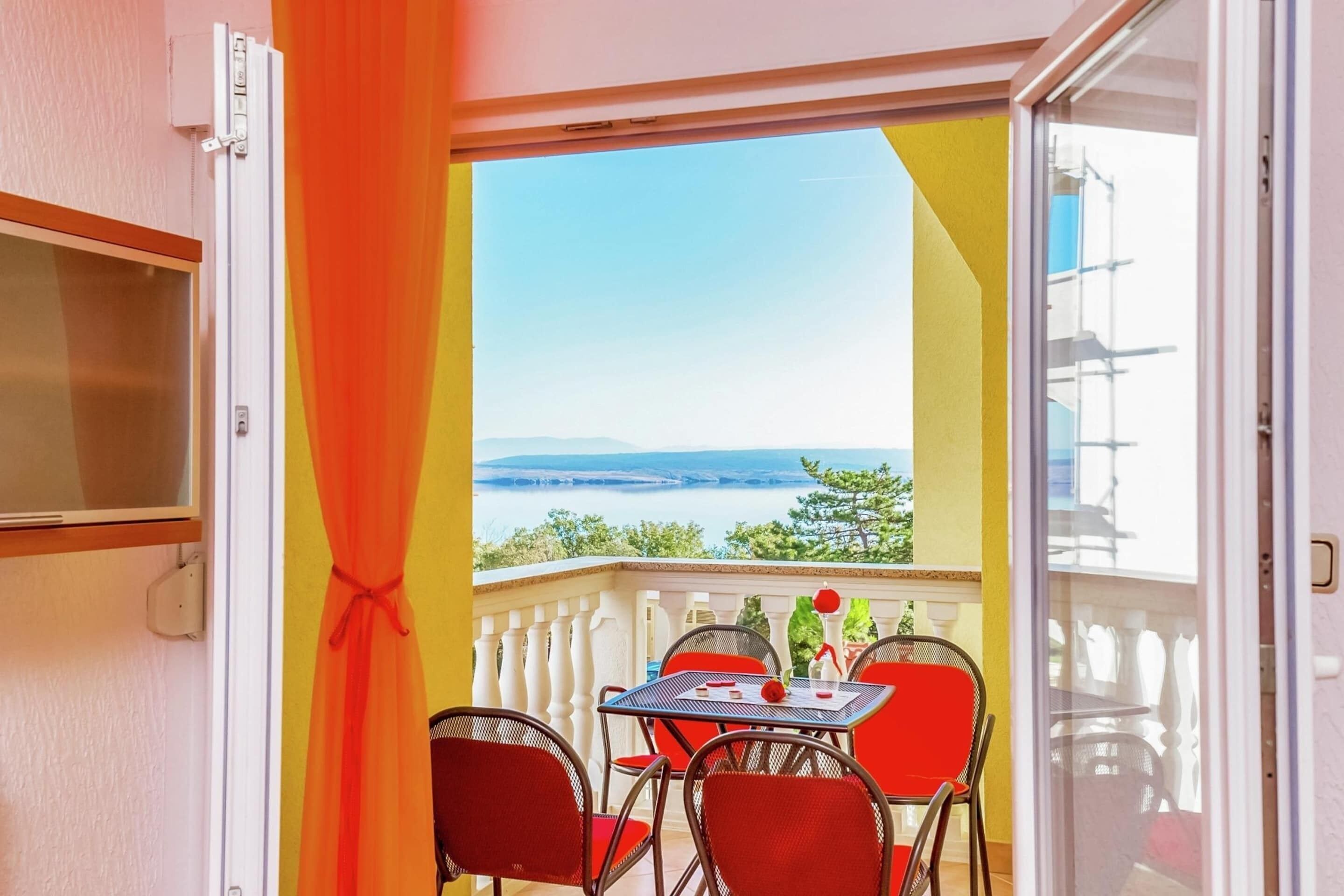 Een balkon met een tafel en stoelen, uitzicht op zee, en een deur met een gordijn.