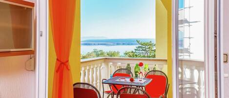 A balcony with a table and chairs, a view of the sea, and a door with a curtain.