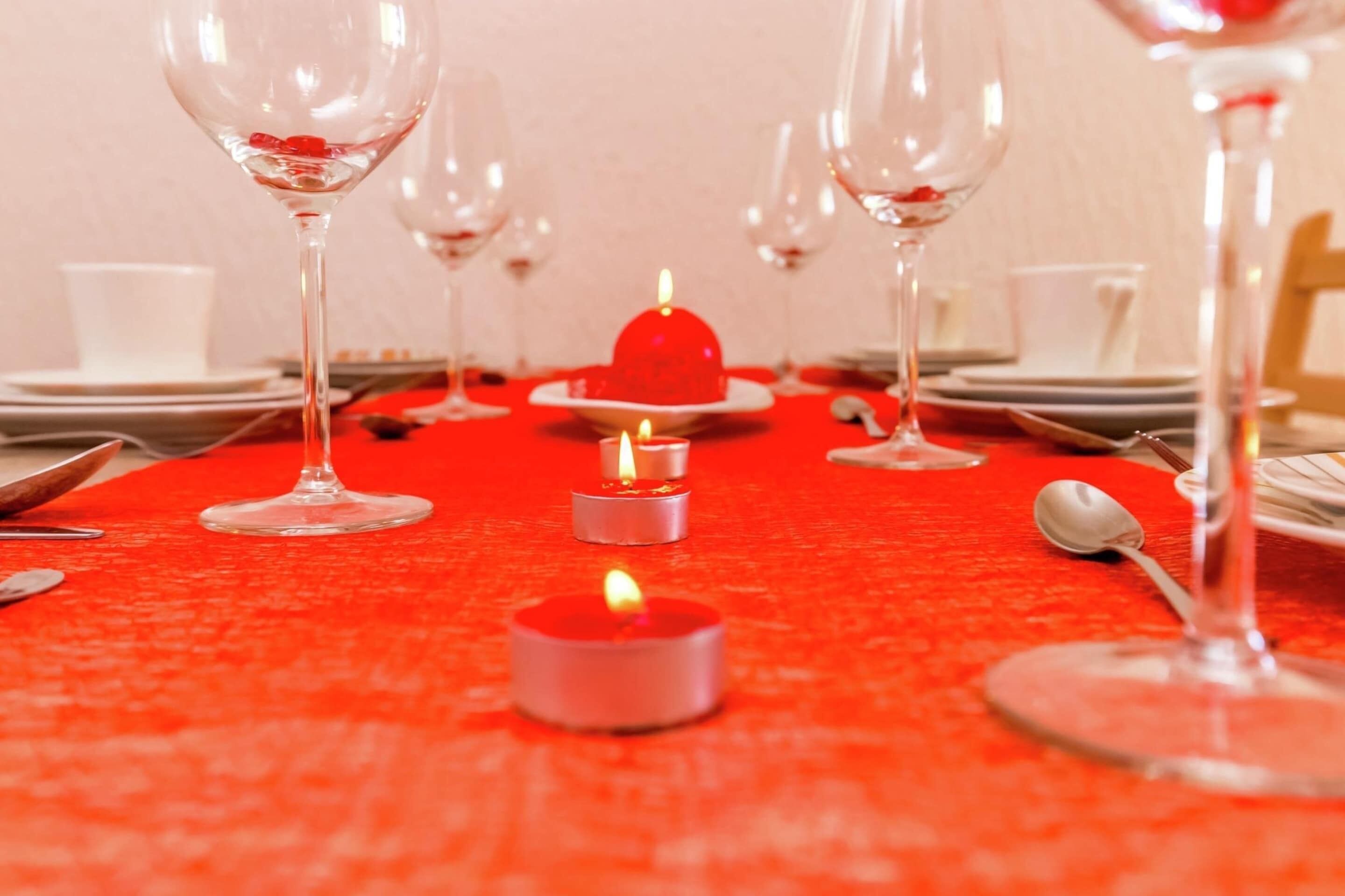 A table set for a meal with wine glasses, plates, and a red tablecloth.