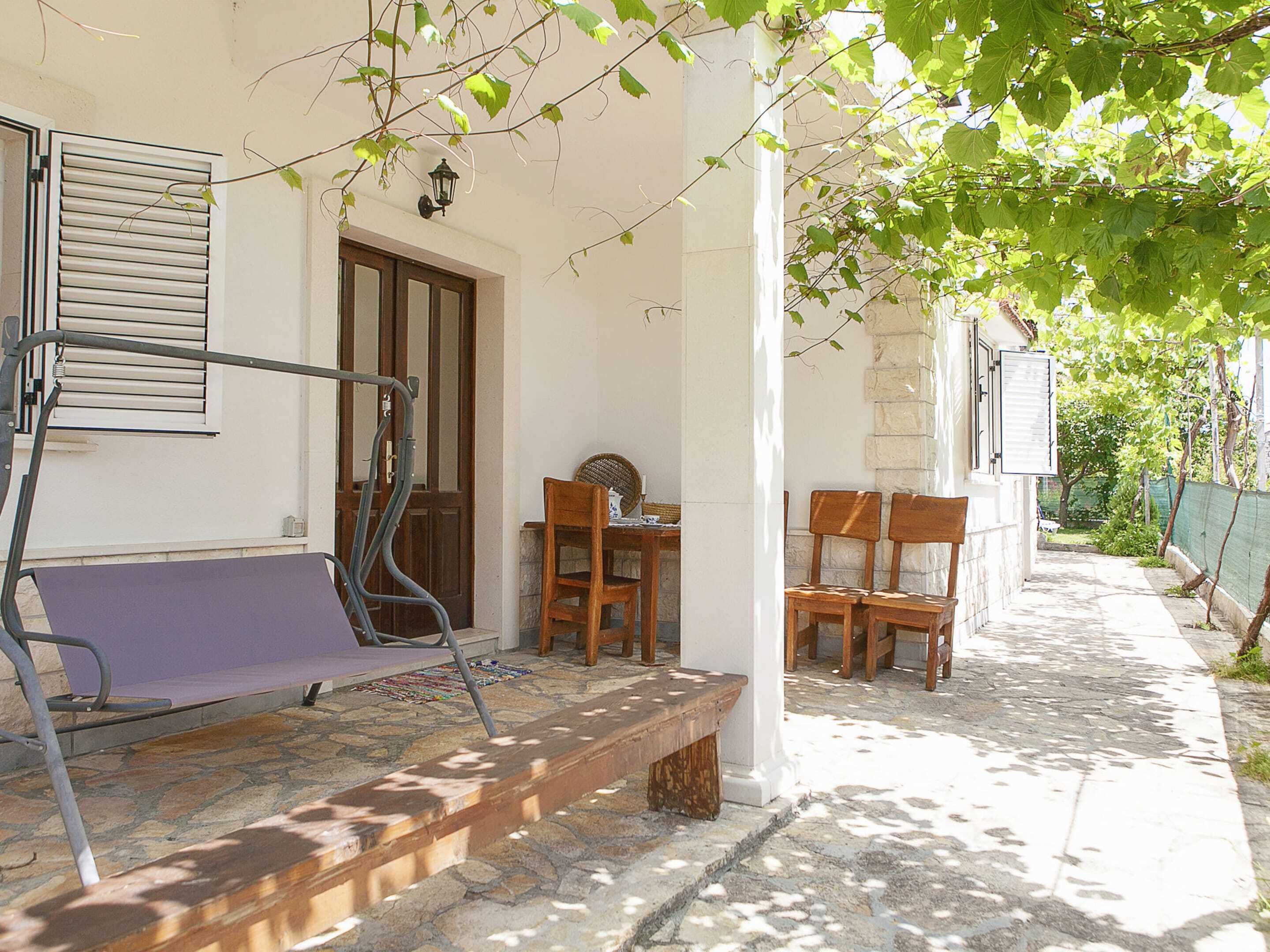 Un espace extérieur dallé de pierres, avec un banc, des chaises en bois et une table.