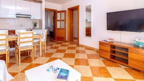 A modern living room with a checkered floor, a dining area with wooden chairs, a TV mounted on the wall, and a kitchen with white cabinets. - Luxurious Apartment in Kvarner by Sea (Crikvenica)