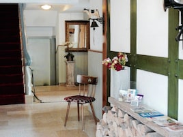 Una habitación con una silla de madera, una mesita con revistas, un espejo y una lámpara fijada a la pared.