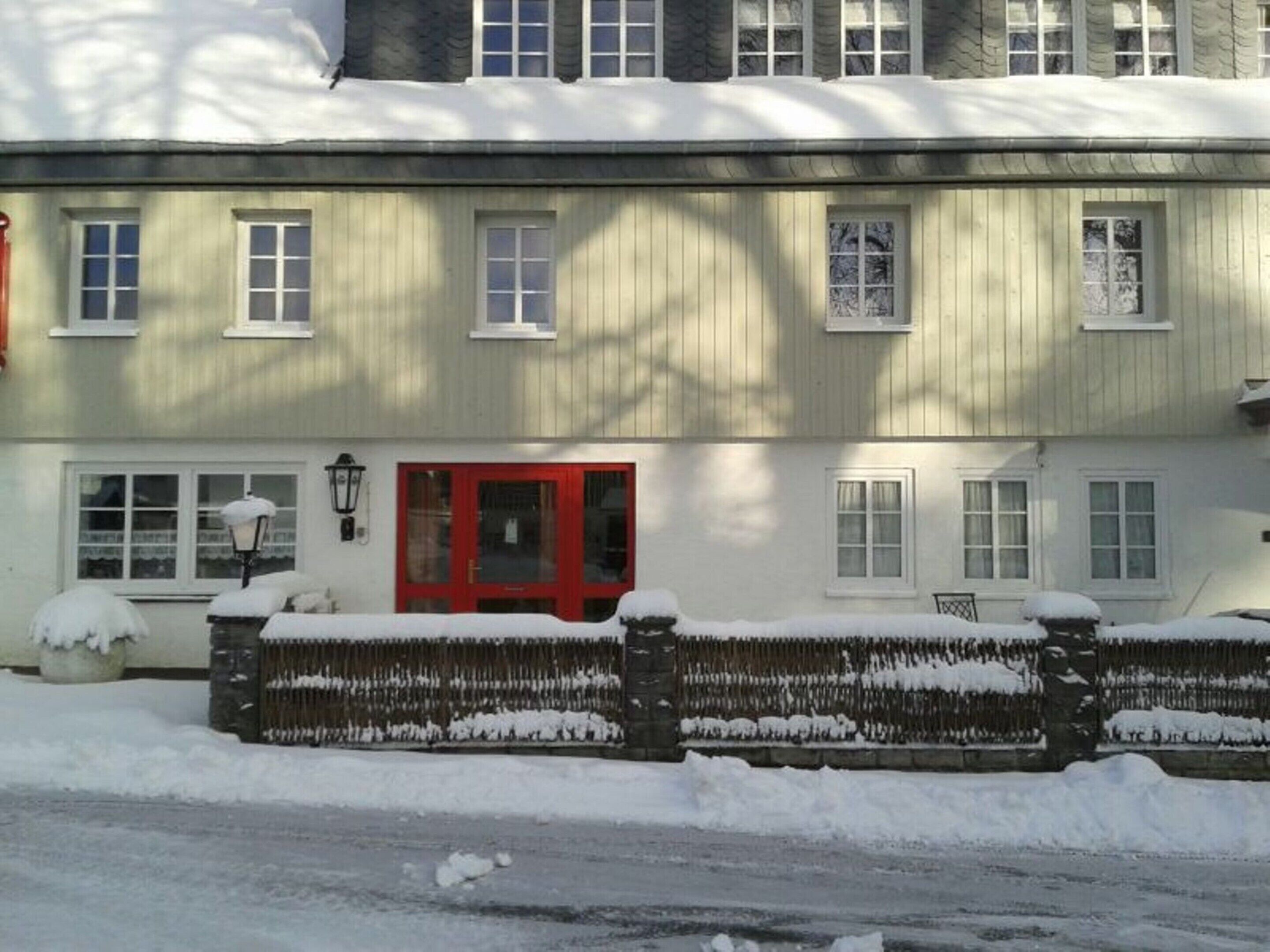 A two-story building with a red door, multiple windows, and a snow-covered exterior.