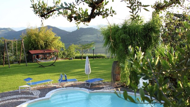 A swimming pool with a tiled deck, surrounded by a grassy area with a hammock and a small building. - Heart of Emilia-romagna Apartment (Modigliana)
