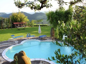 A swimming pool with a tiled deck, surrounded by a grassy area with a hammock and a small building. - Heart of Emilia-romagna Apartment (Modigliana)