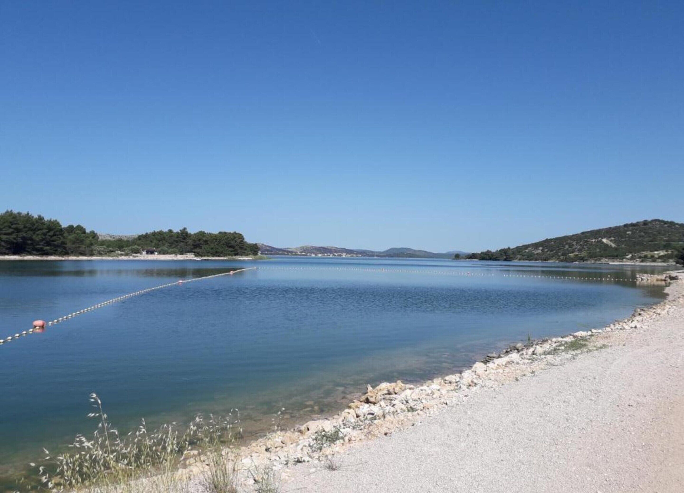 A clear view of a lake with a sandy beach and a rope barrier.
