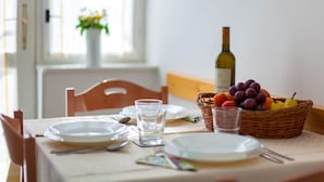 Une table à manger dressée avec des assiettes, des couverts, des verres, une bouteille de vin et un panier de fruits.