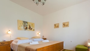 Une chambre à coucher avec un lit en bois, deux tables de chevet avec des lampes, un fauteuil vert et des œuvres d’art accrochées aux murs.