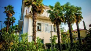 Un bâtiment à deux étages doté d’un balcon, entouré de palmiers et de verdure.