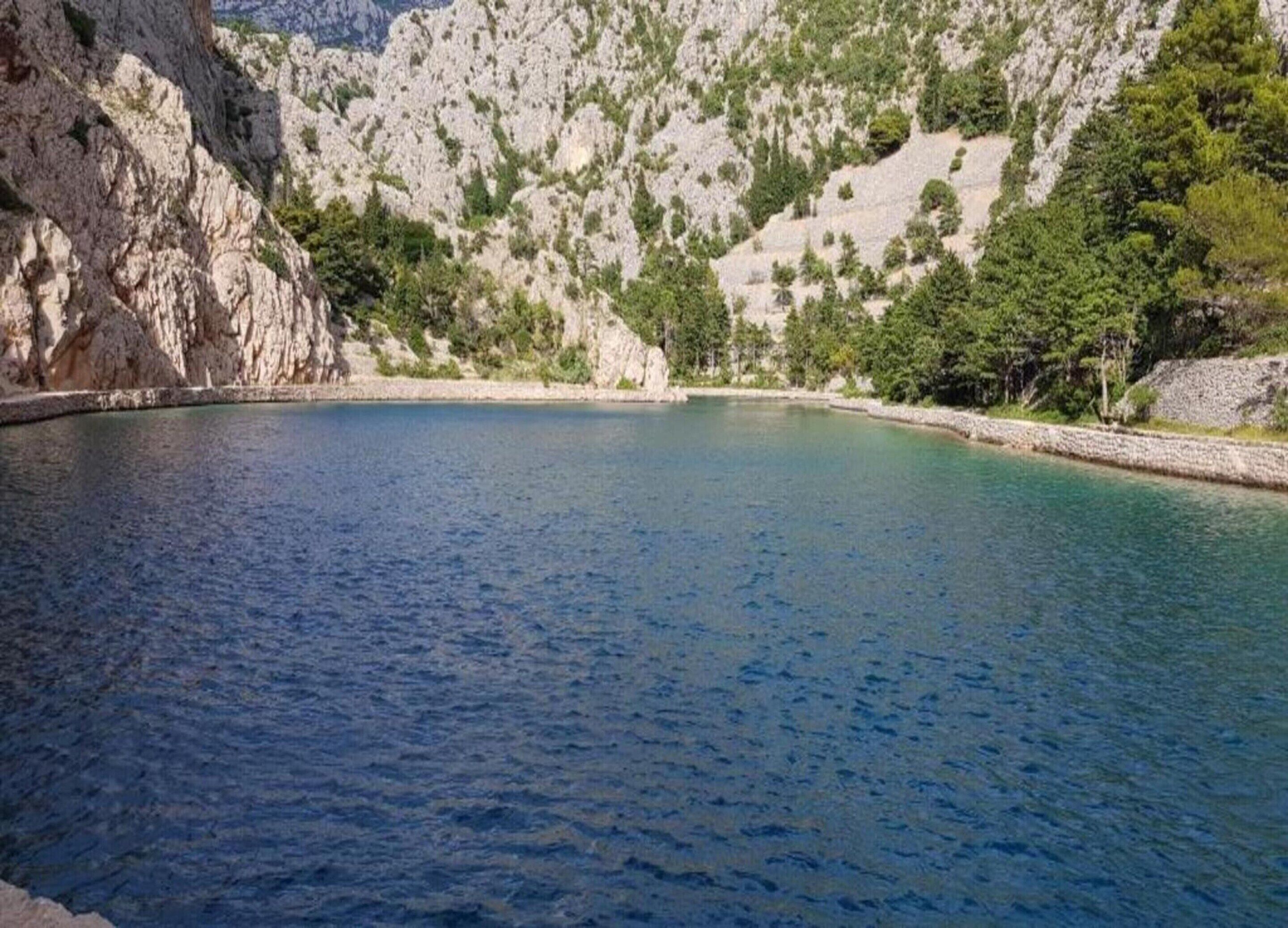 Un lago blu e cristallino circondato da scogliere rocciose e vegetazione rada.