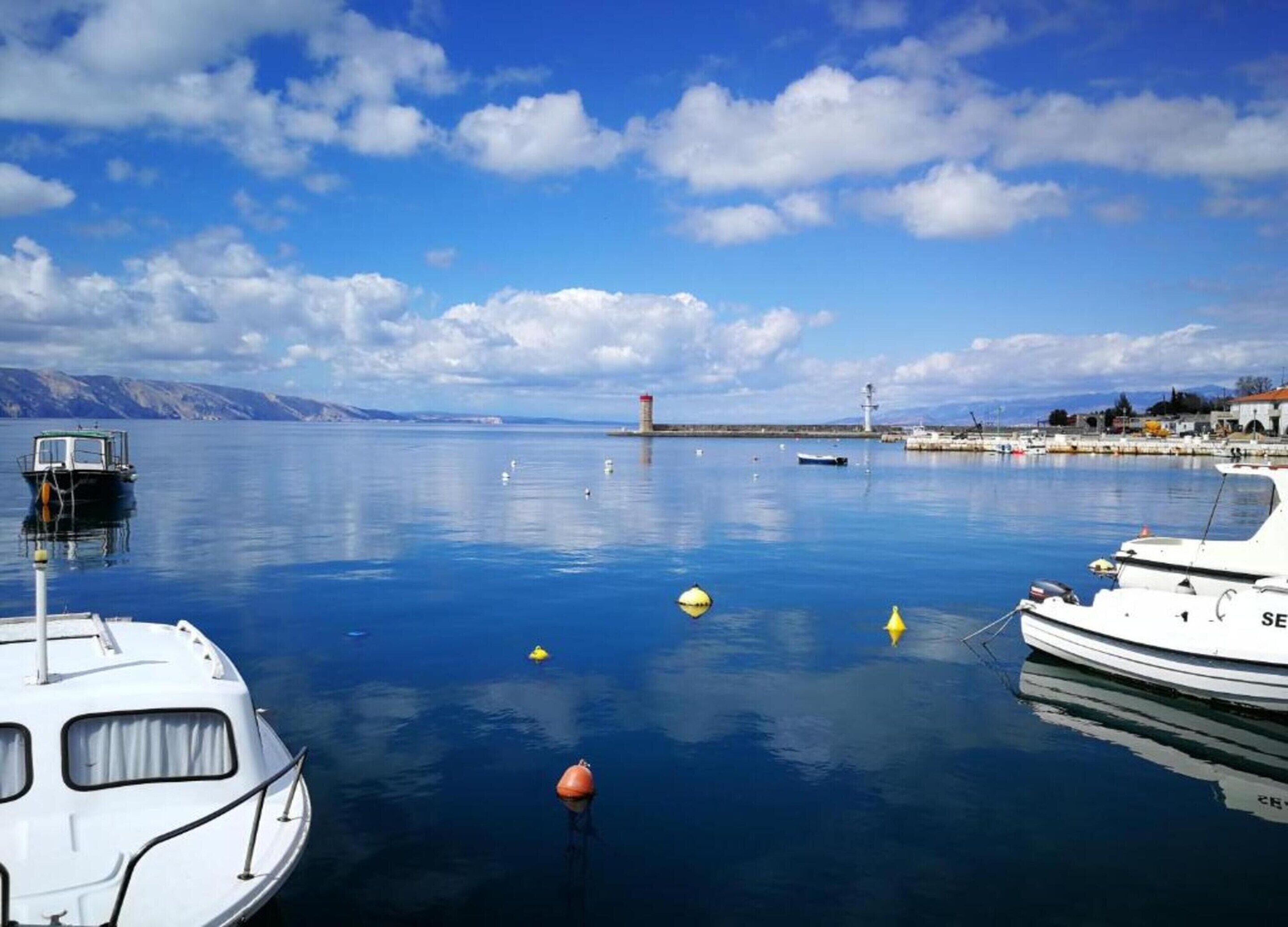 A calm harbor with boats docked, a lighthouse, and a clear sky.