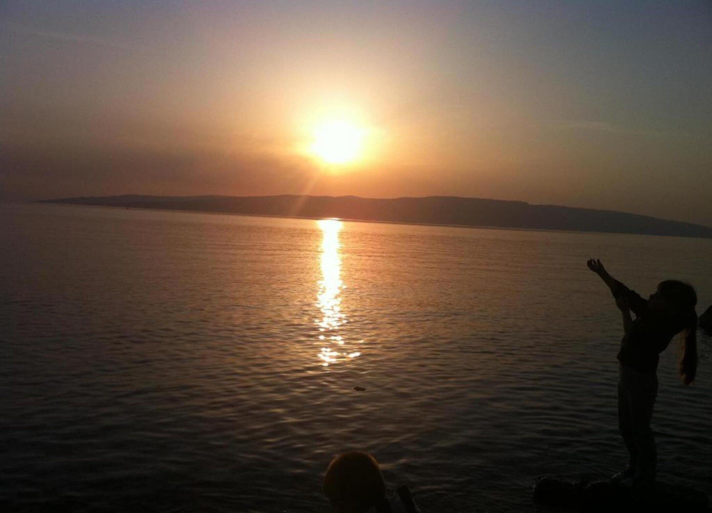 Un coucher de soleil sur une étendue d’eau calme, avec la silhouette d’une personne debout sur la rive.