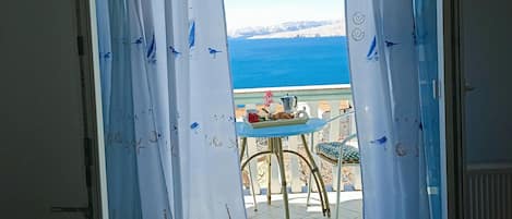 Un balcón con una mesa lista para el desayuno, con vistas a un paisaje marítimo y montañas distantes.