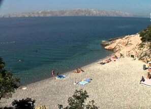 A beach with clear blue water, sandy shore, and rocky cliffs in the background. - Adorable Apartment With Pool & Terrace With Sea View (Senj)