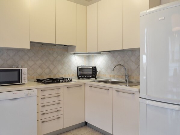 Una cocina moderna con armarios blancos, un microondas Bosch, una estufa a gas, un tostador y un refrigerador.