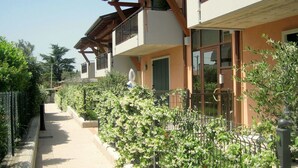 A row of modern two-story buildings with balconies, surrounded by a metal fence and lush greenery. - Elegant Holiday Home in Lazise with Swimming Pool near Lake (Lazise)