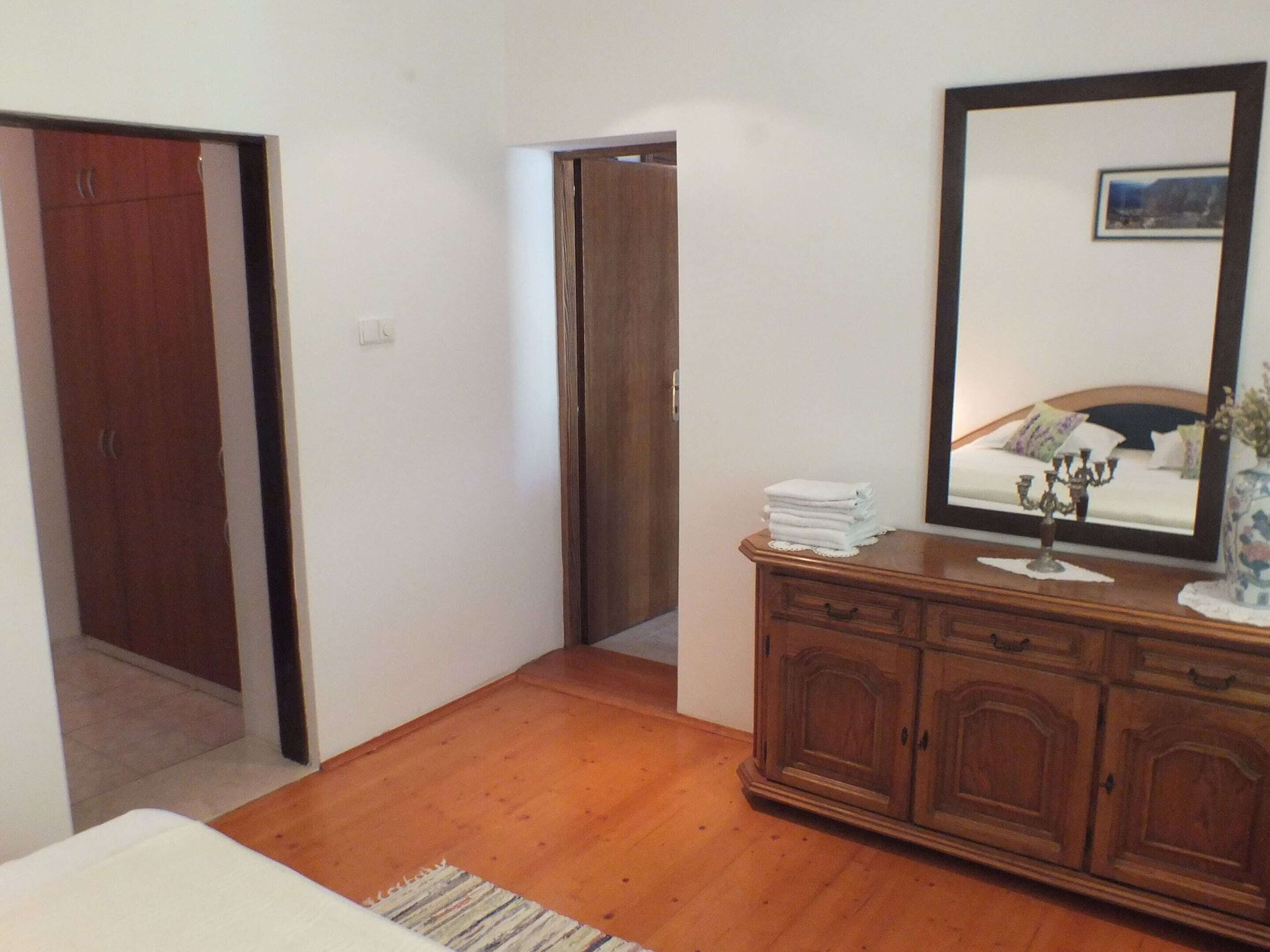 A bedroom with a wooden floor, a bed, a dresser with a mirror, and a door leading to another room.