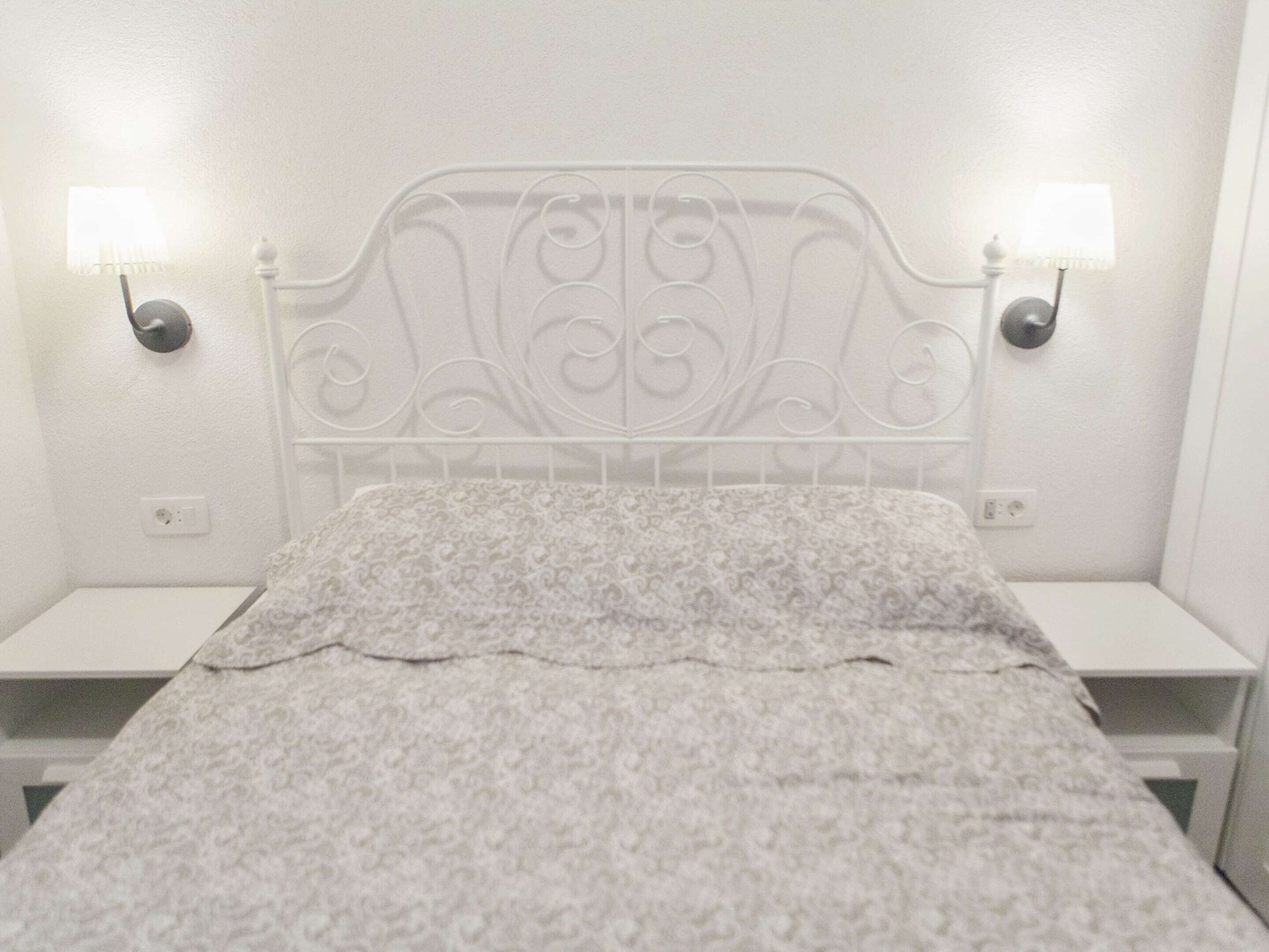 A white metal bed frame with a decorative headboard, two bedside tables, and a patterned bedspread.