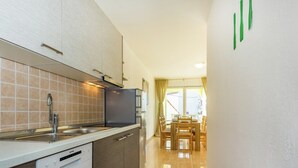 A compact kitchen with a dishwasher, a sink, and a refrigerator. There is a dining area with a table and chairs. - Villa in Croatia Near Beach With Pool (Crikvenica)