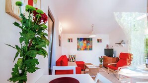 Un salon moderne avec un canapé blanc, des coussins rouges, une table basse en bois et une grande plante.
