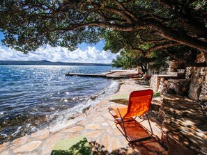 Un sendero de piedra conduce a una zona de estar junto al lago, con una silla roja y una mesa, con vistas al agua.